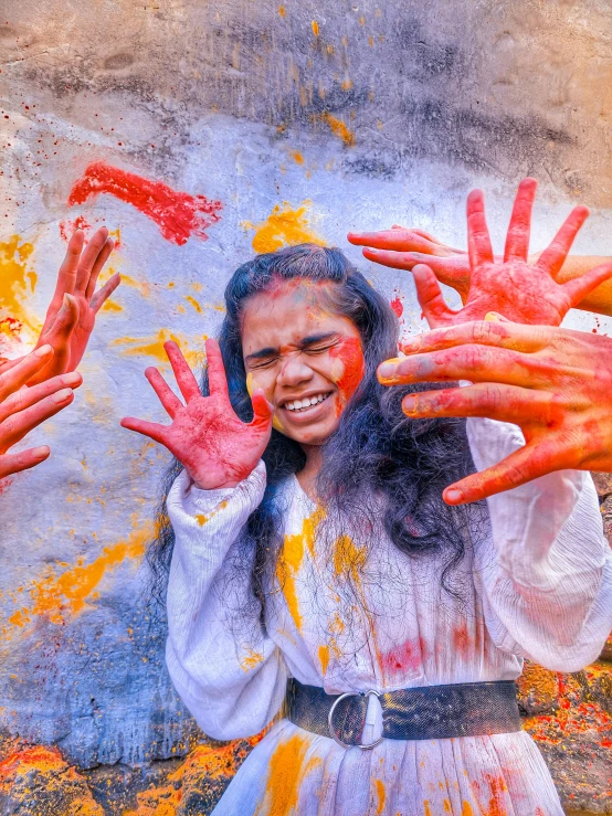 an indian girl poses in front of a mural with colorful paint on her hands