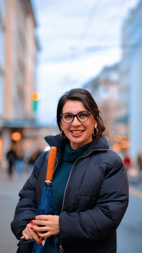 woman with glasses standing on city street next to light post