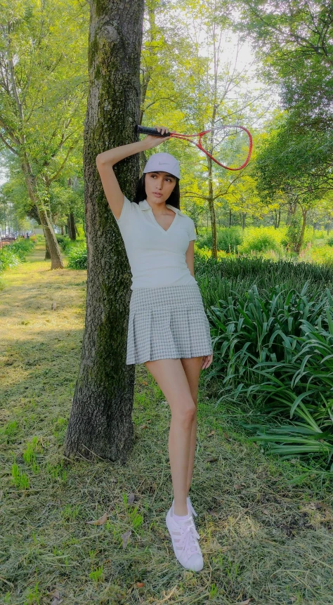 a young woman holding a tennis racquet leaning against a tree