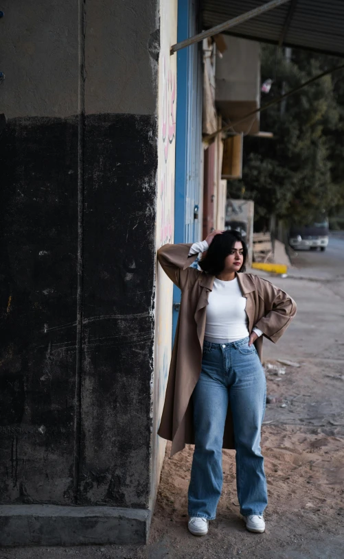 a woman in high rise jeans leans against a building