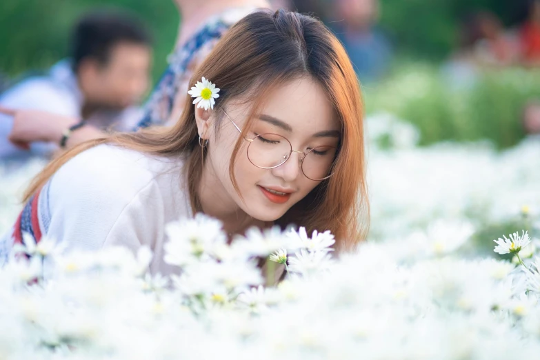 a woman wearing glasses sitting in the middle of a field of flowers