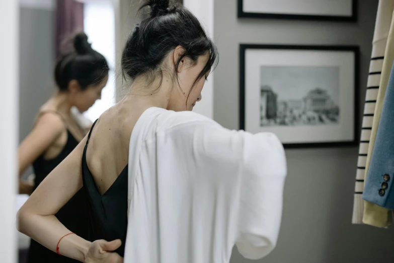 woman in bathroom putting on her shirt while looking into mirror