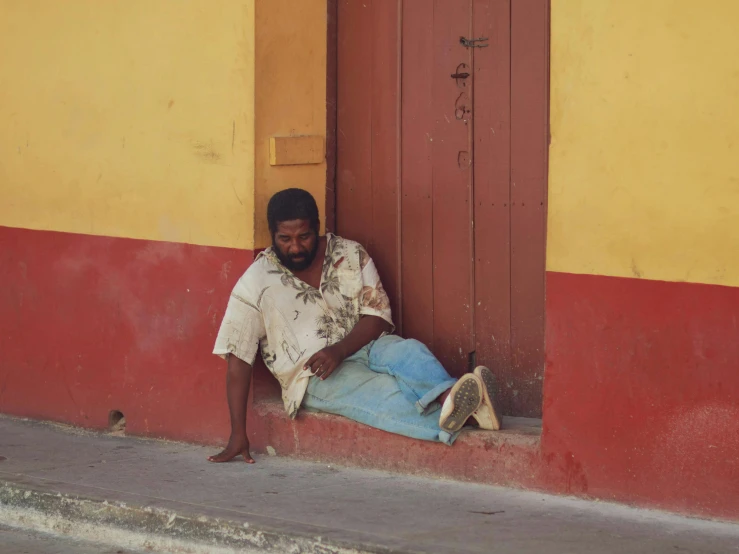 a man sitting on the curb leaning against a yellow wall