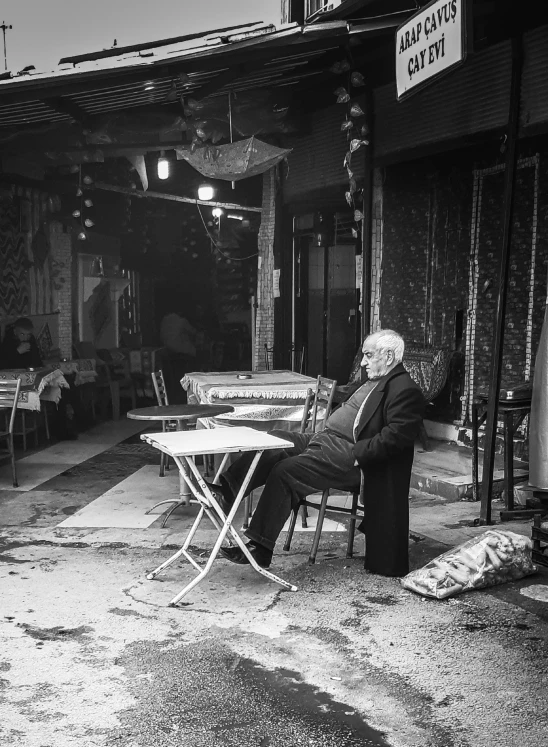 black and white image of person sitting in front of restaurant