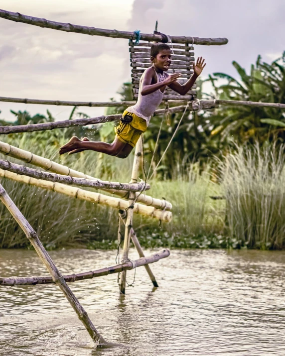 a boy on stilts jumps off a high wooden bridge over the water