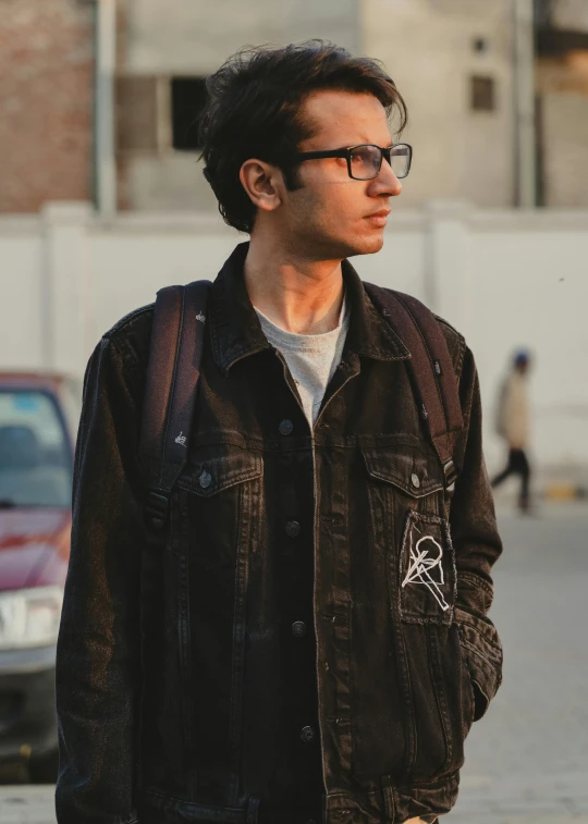 man with glasses standing next to a brick wall