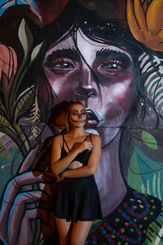 a person in a black outfit standing near a mural