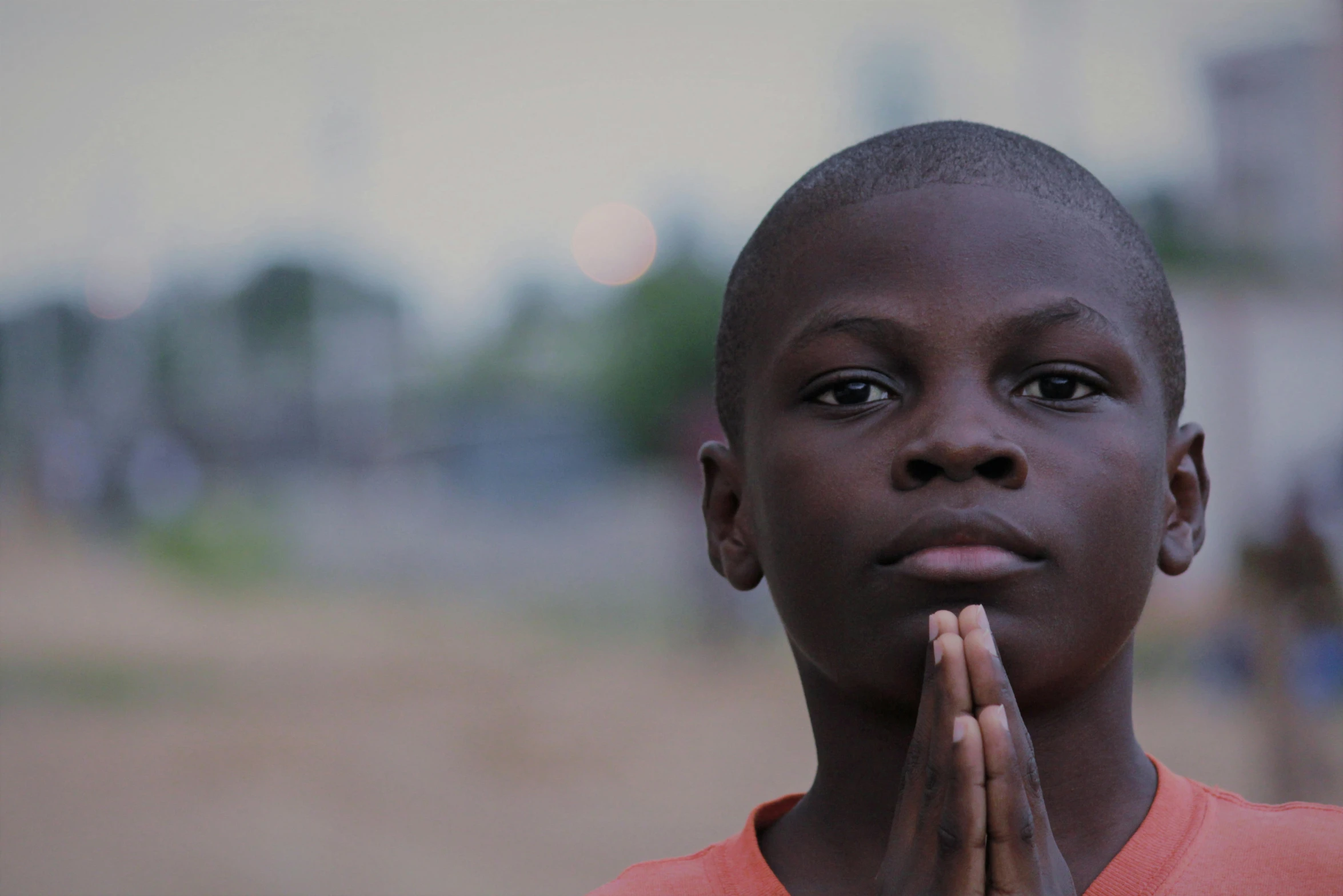 a black girl with an orange shirt on praying