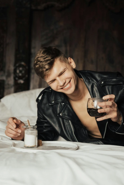 a young man laying in bed holding a drink