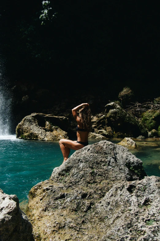 a woman is sitting on rocks next to a waterfall