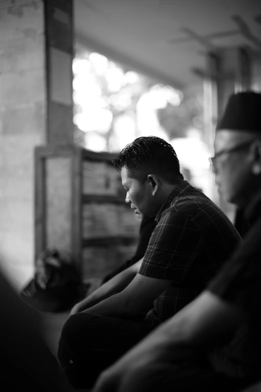 two men sitting in front of a window in black and white