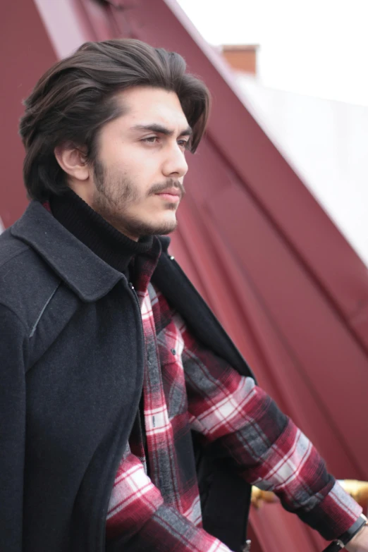 a man wearing a plaid shirt next to a wall