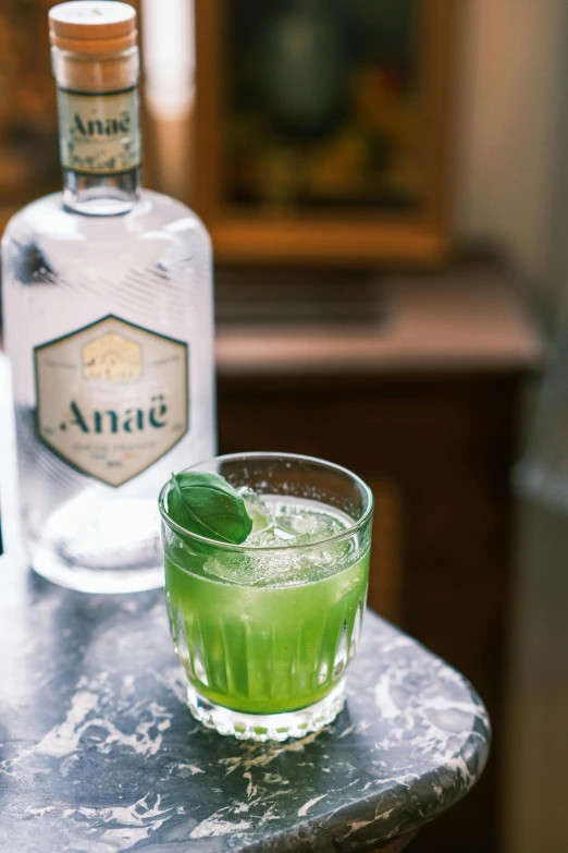 a bottle of gin sits next to a glass filled with a green drink