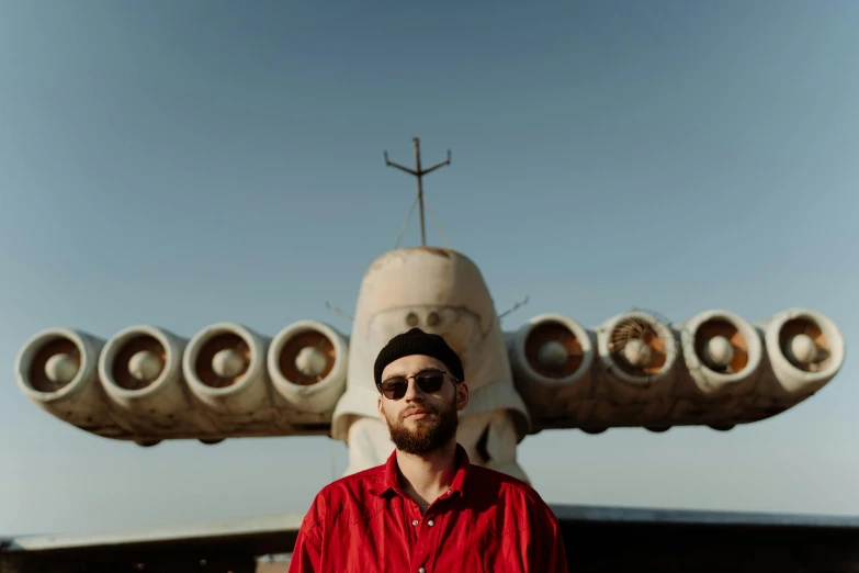 a man with dark sunglasses poses in front of a model plane