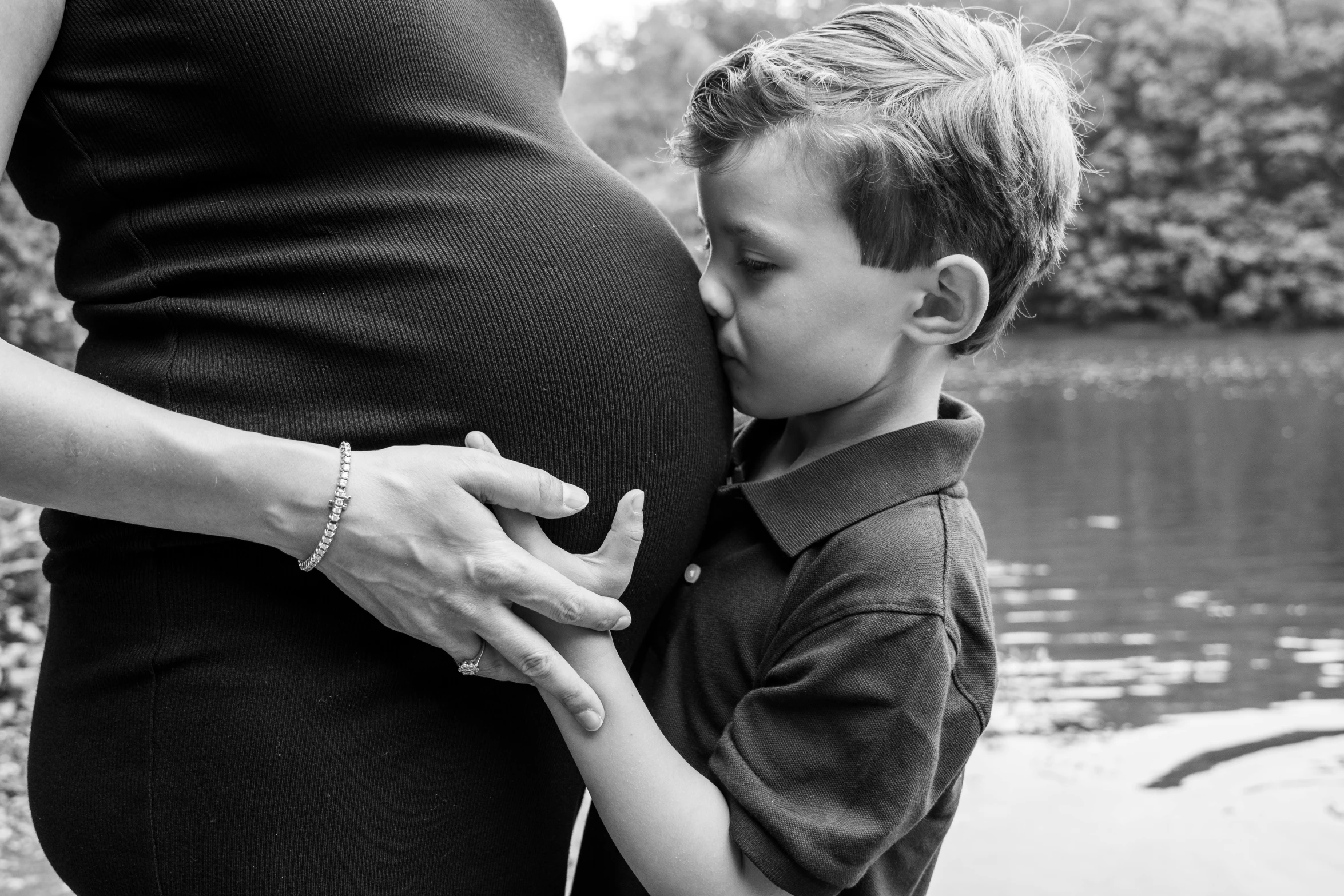 a pregnant woman and child on the side of a lake