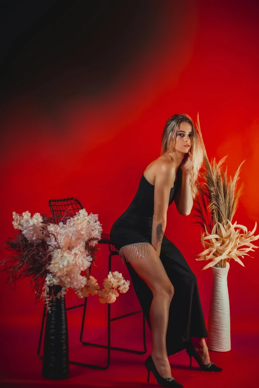 a woman poses next to two flowers and a chair