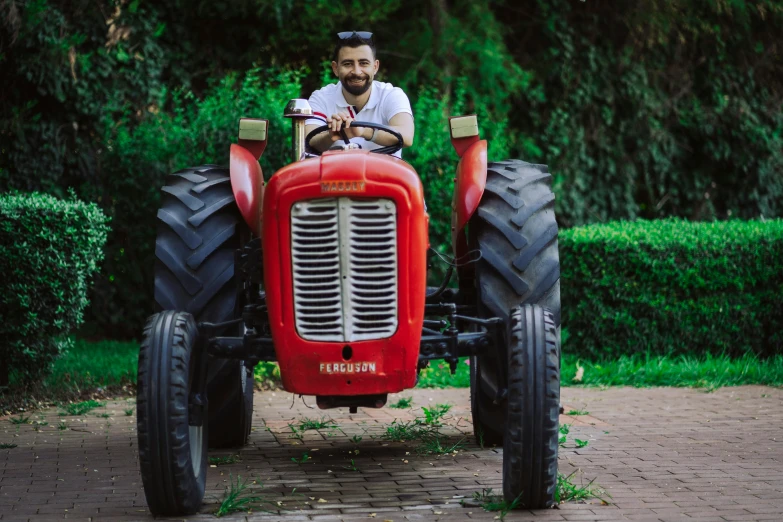 a man sits on an old tractor in a driveway