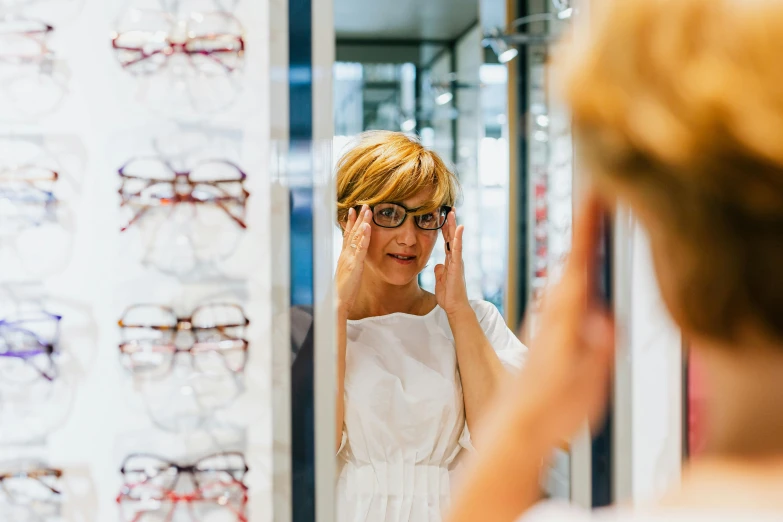 a woman is reflected in a mirror while she looks at glasses