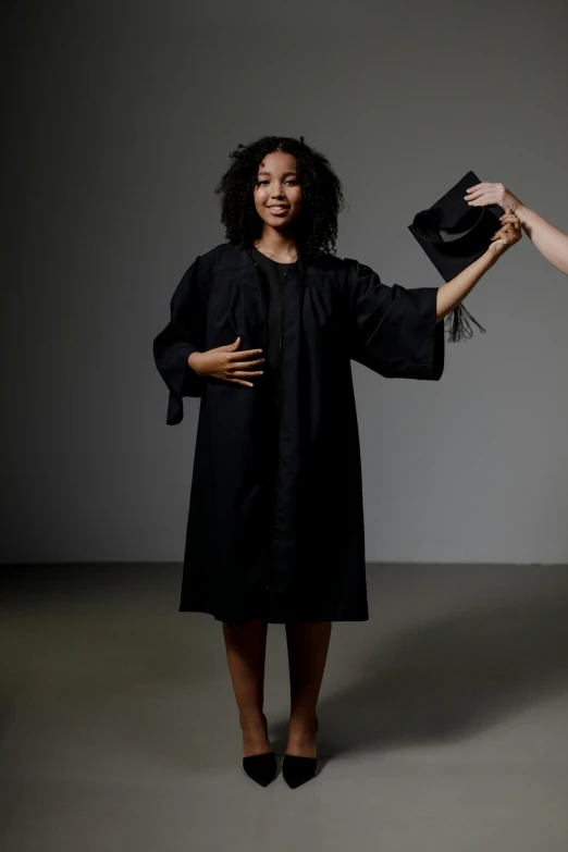 a smiling woman in a black dress holds a hat