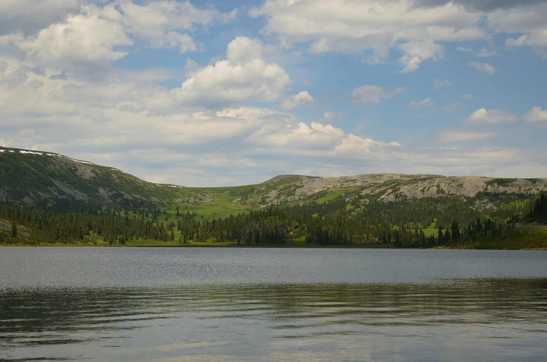 a body of water next to mountains under a cloudy blue sky