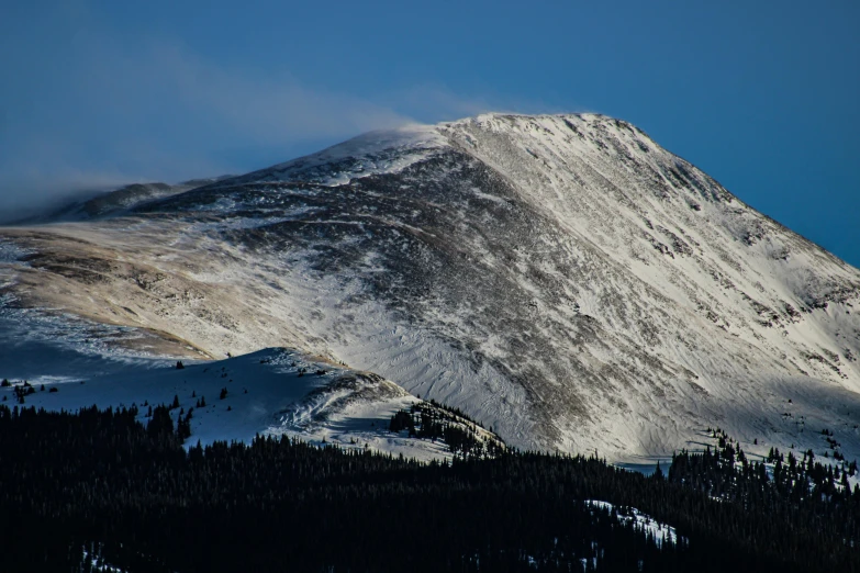 a large snow covered mountain with pine trees below