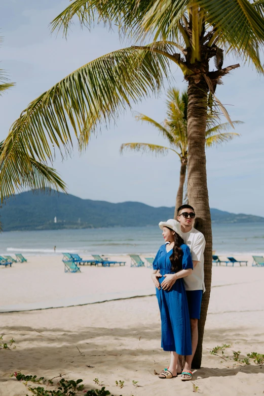 a pregnant woman stands on a beach by a palm tree