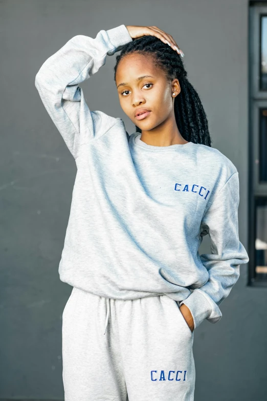 a woman stands wearing a grey sweat suit and smiling