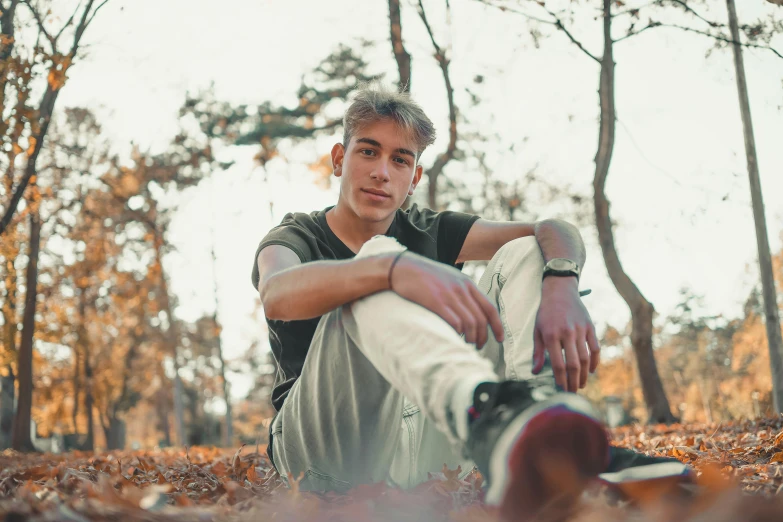 a young man sitting on the ground in the woods