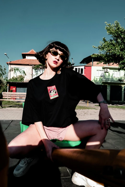 a girl in sunglasses and a black shirt sits on a bench