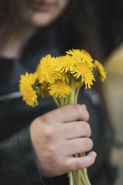 a hand holding some yellow flowers out side