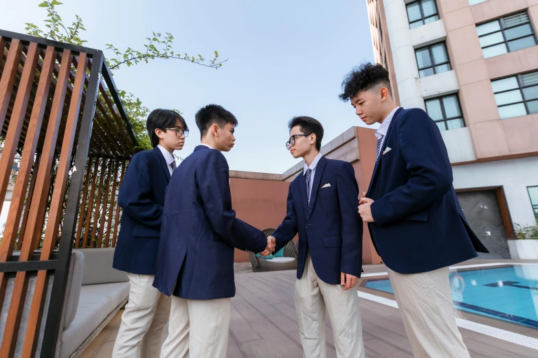 three men dressed in blue suits shaking hands next to a swimming pool