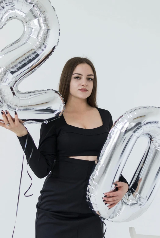 a woman in a black dress holding two silver balloons