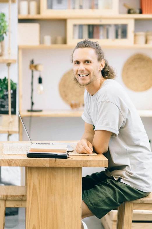 a man sitting at a desk smiling while working on a laptop computer