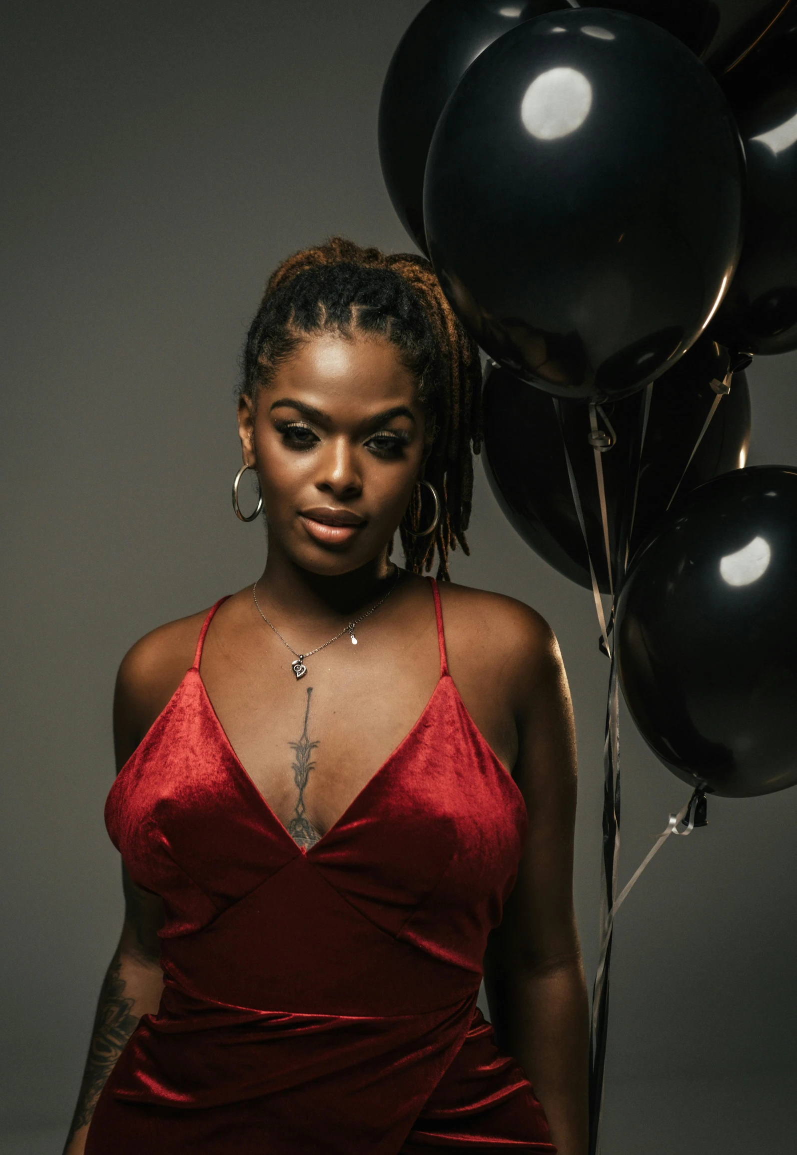 a woman in red dress standing with several black balloons