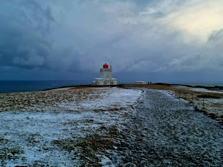 a road running past a white lighthouse surrounded by snow