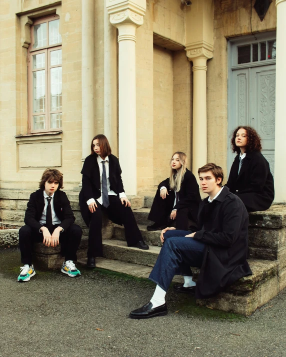 five people sitting on stairs outside a large building