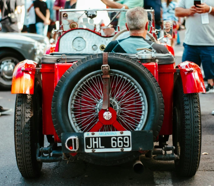 an old fashioned pedal car sitting on the street with a group of people