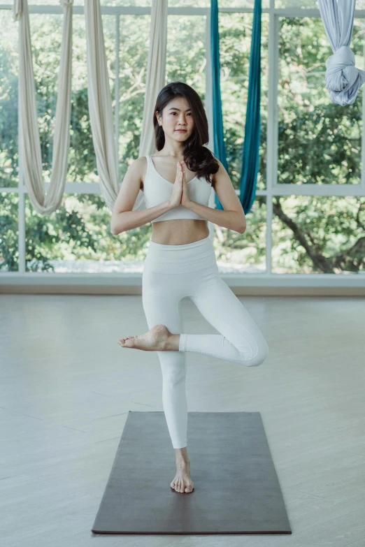 an asian girl in white poses on a yoga mat