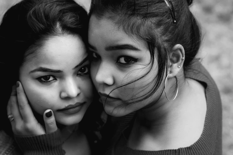 two girls in gray sweaters pose together, one with her hands on the face