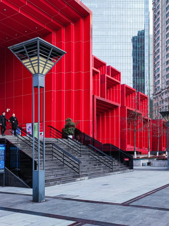 a street lamp stands on the sidewalk near some stairs and a large red wall