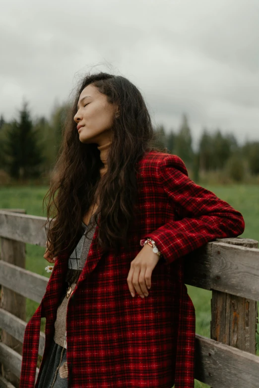 woman wearing plaid jacket leaning against wooden fence