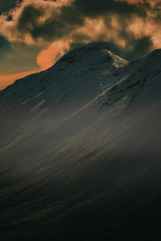 the clouds cover a snowy mountain with red light in the sky