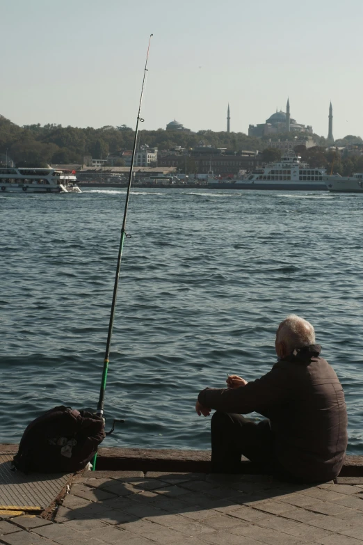 the man is fishing from the pier near the water