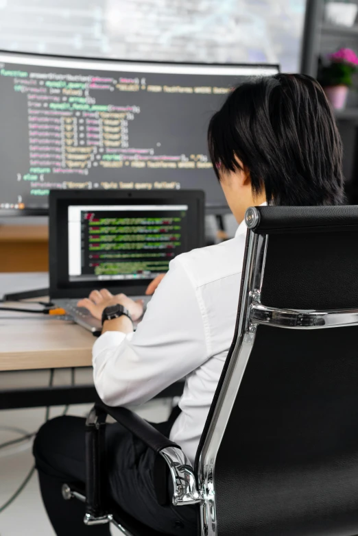 an asian man sits at a desk with a laptop and computer screen