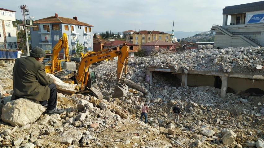 a construction worker digs through rubble next to his home