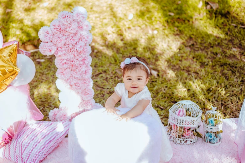 a baby girl sitting on her pink teddy bear at a pink and white birthday party