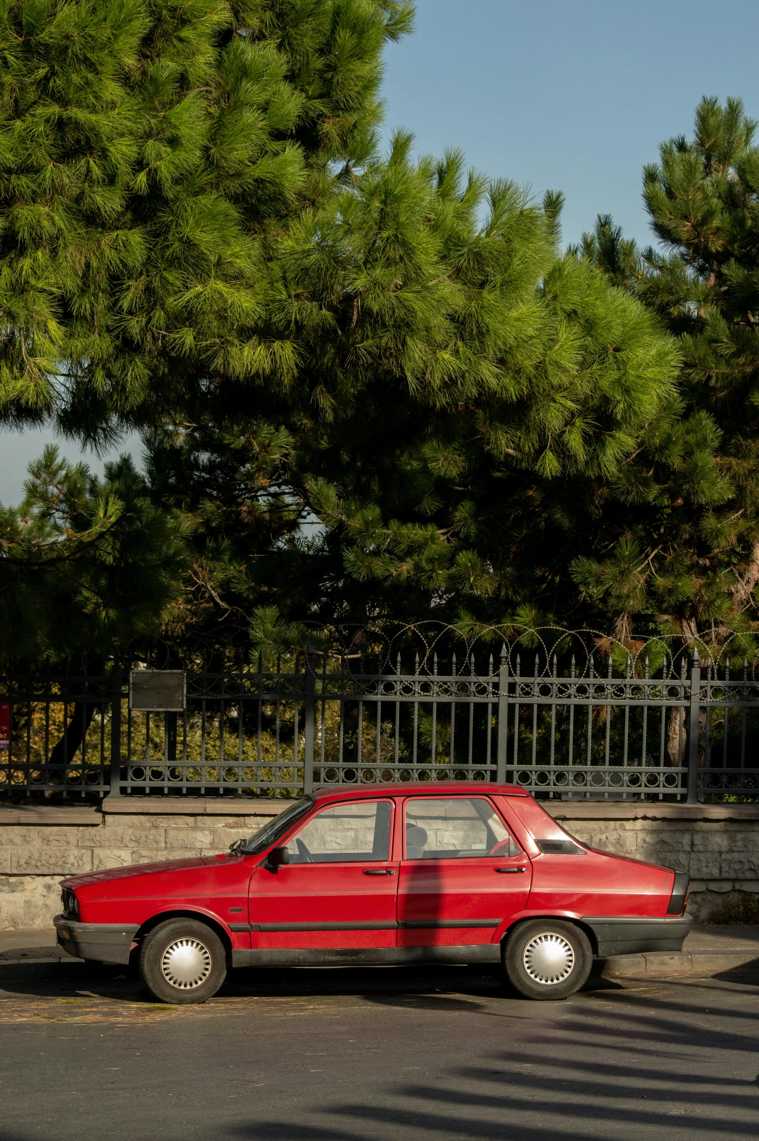 a small red car parked along the side of a road next to a stone wall