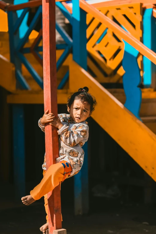 the little child is standing on the red pole