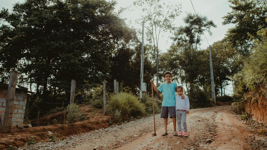 a man and girl stand in the dirt beside a road with trees