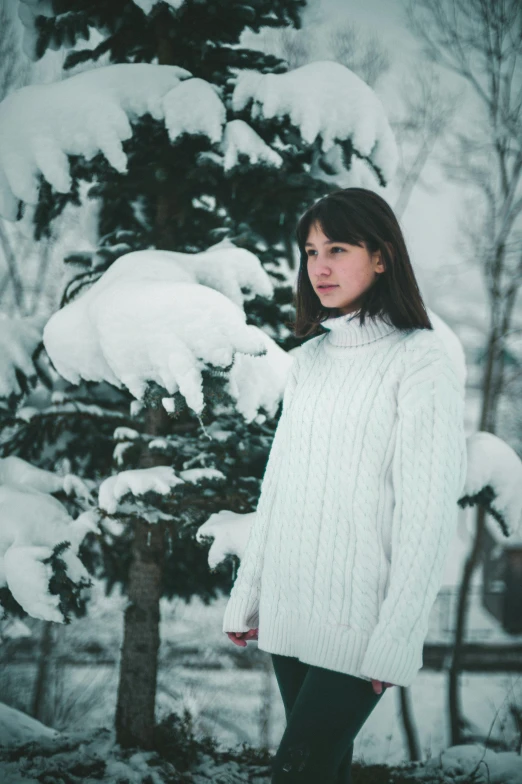 a girl stands in front of a snowy tree